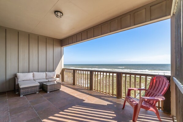 A balcony with a view of the ocean, a wicker sofa, and a red chair. - Delightful escape with direct beach access, WiFi, furnished deck, & full kitchen (Gulf Shores)