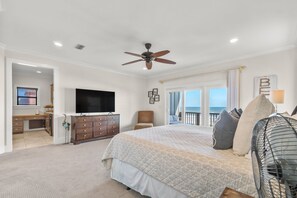 Ein Schlafzimmer mit Bett, Deckenventilator, Fernseher, Kommode und Blick auf den Ozean.