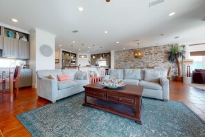 A spacious living room with a large sectional sofa, a wooden coffee table, and a kitchen in the background. - Delightful escape with direct beach access, WiFi, furnished deck, & full kitchen (Gulf Shores)