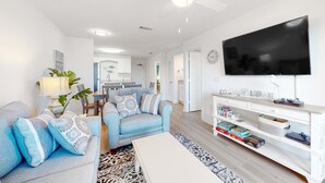 Ein modernes Wohnzimmer mit Sofa, Couchtisch und Fernseher. Im Hintergrund ist eine Küche zu sehen.