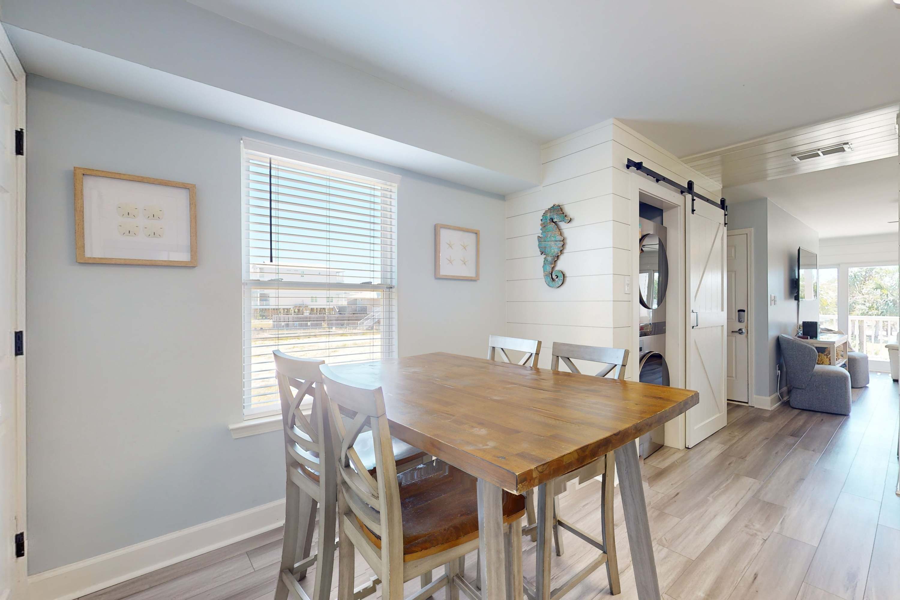 A dining area with a wooden table and white chairs, a sliding barn door, and a seahorse wall decoration.