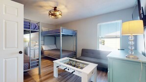 Quarto compacto com beliches, mesa de pebolim, sofá e luminária.