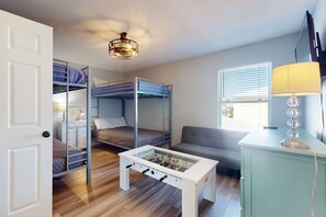 A compact room with bunk beds, a foosball table, a sofa, and a lamp. - Chic, updated home with high-speed WiFi, AC, & W/D - nearby beach access (Gulf Shores)