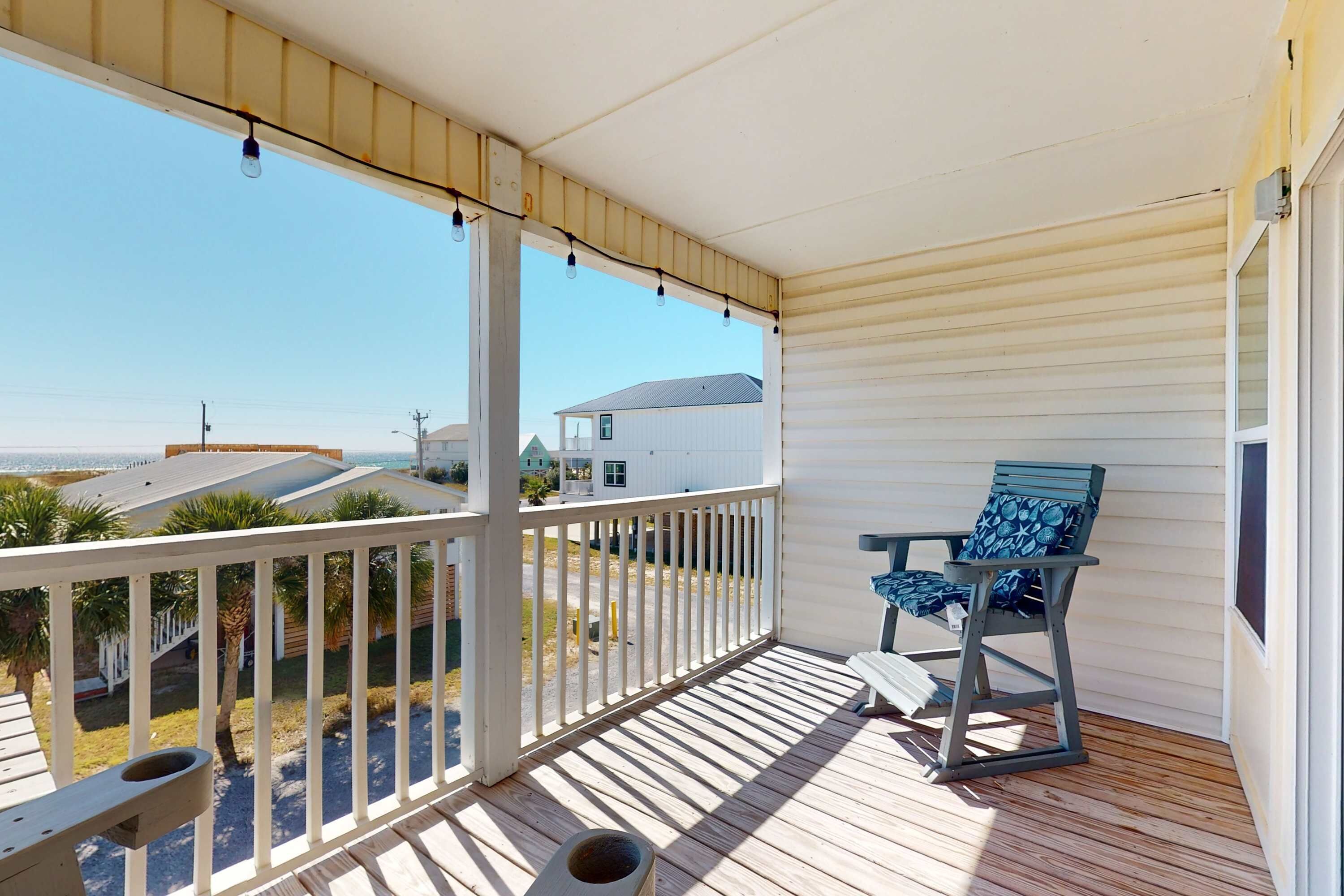 Een overdekt balkon met uitzicht op het strand, een houten tafel, een stoel en een kleine prullenbak.