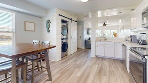 Cozinha moderna com ilha central, área de refeições com mesa de madeira e lavanderia com máquina de lavar.
