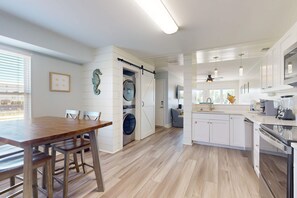 A modern kitchen with a central island, a dining area with a wooden table, and a laundry room with a washing machine. - Chic, updated home with high-speed WiFi, AC, & W/D - nearby beach access (Gulf Shores)