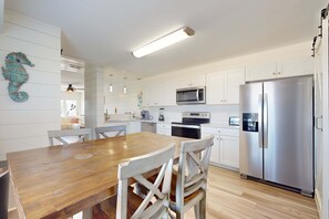 A modern kitchen with white cabinetry, a wooden dining table, and a stainless steel refrigerator. - Chic, updated home with high-speed WiFi, AC, & W/D - nearby beach access (Gulf Shores)