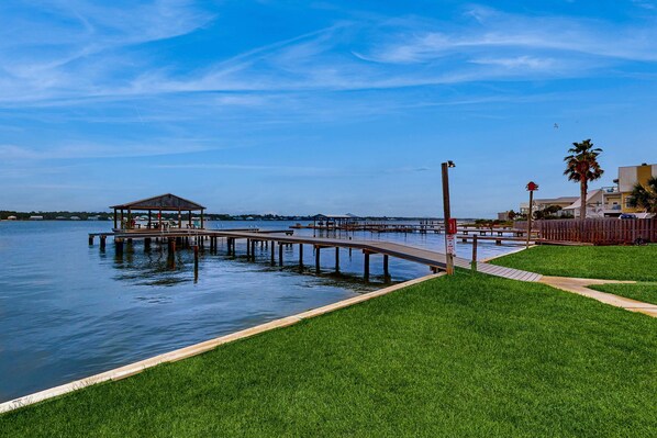 Un parque junto al agua con un quiosco, un muelle de madera y una zona verde.