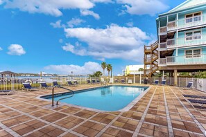 A pool area with lounge chairs, a staircase, and a building with balconies. - Gulf-view condo with pool, balcony, & central AC - walk 50 feet to deeded beach (Gulf Shores)