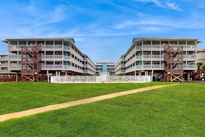 A symmetrical building with multiple balconies, a central walkway, and a fenced area. - Gulf-view condo with pool, balcony, & central AC - walk 50 feet to deeded beach (Gulf Shores)