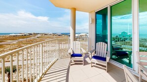 Ein Balkon mit Blick auf den Strand, weißen Stühlen und einer Glastür.