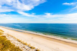 En strand med klar himmel, sandstrand och ett staket längs kanten.