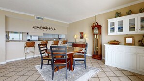 Uma sala de jantar com uma mesa redonda e cadeiras, uma cozinha ao fundo e um armário branco com portas de vidro.