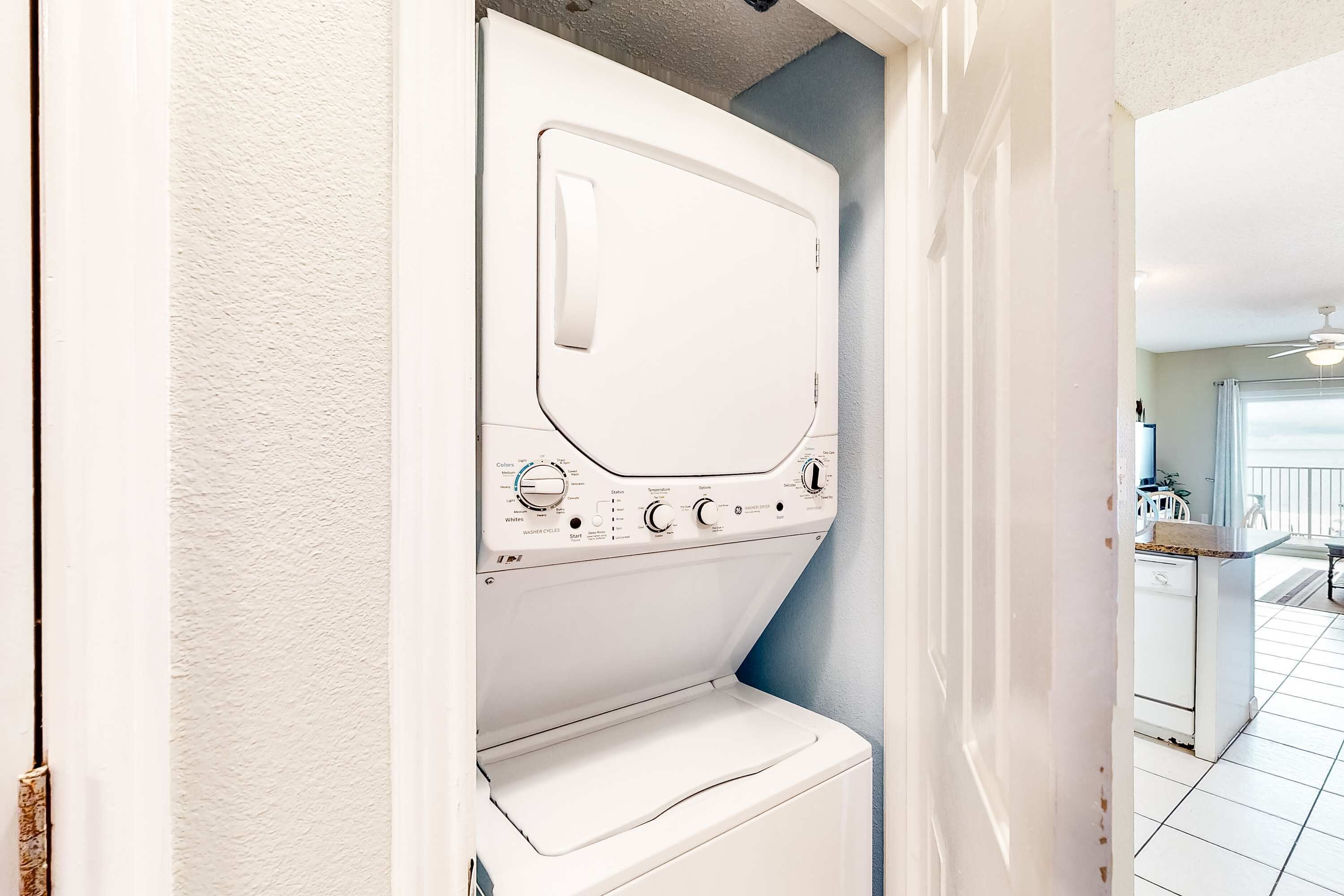 A laundry room with a front-loading washer and dryer, a ceiling fan, and a view of a kitchen area.