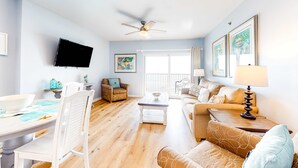 A living room with a flat-screen TV, ceiling fan, dining table, and a sofa. - Amazing Condo in Gulf-Front Condo Featuring a Shared Pool, Free WiFi, Central AC (Gulf Shores)