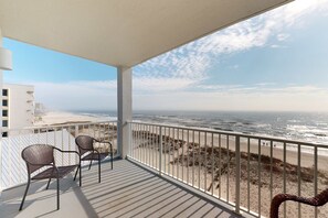 Ein Balkon mit Blick auf den Strand, zwei Stühle und einem Geländer.