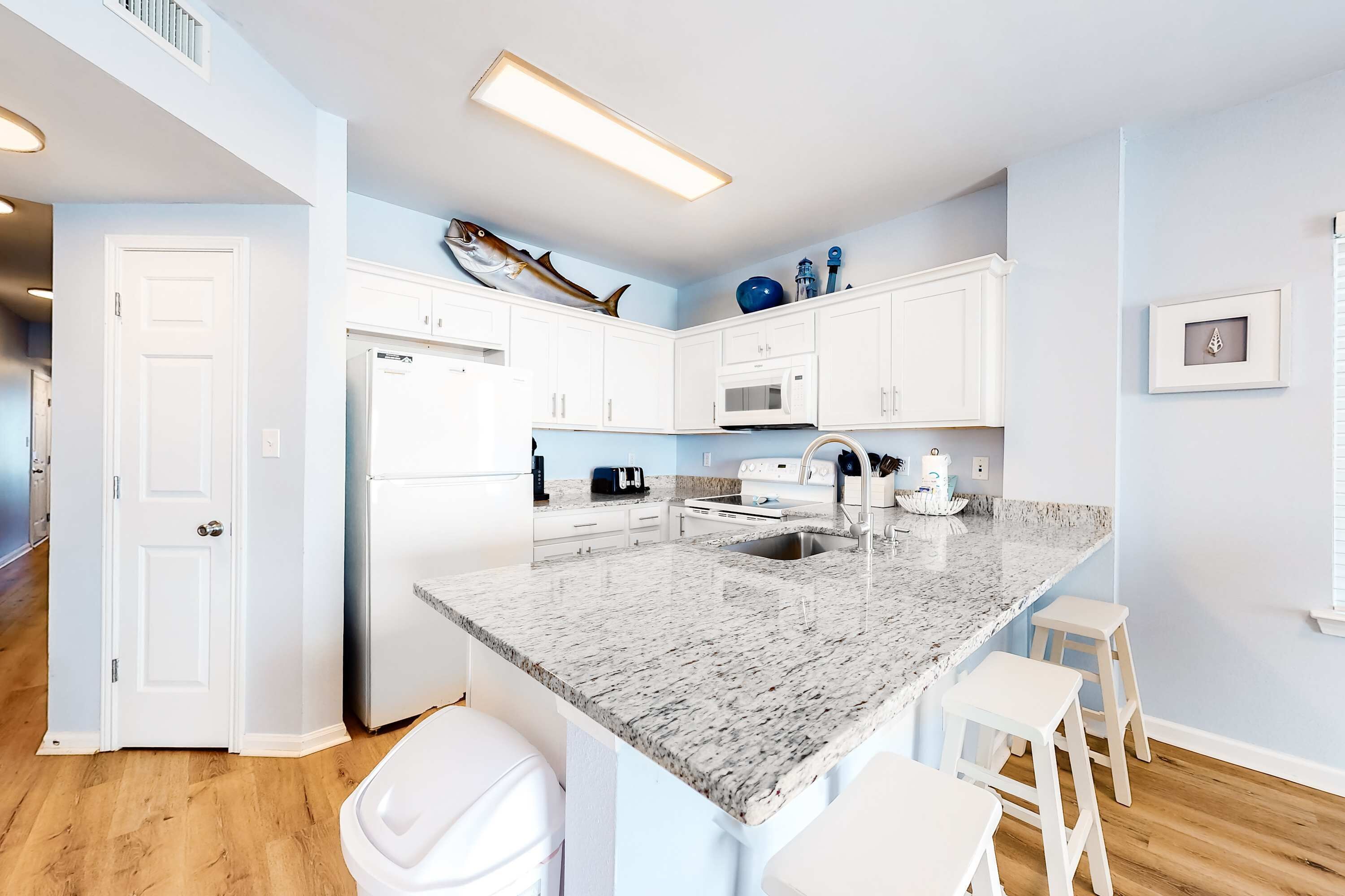Una cocina moderna con armarios blancos, encimera de granito y una isla grande con taburetes.