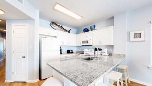 A modern kitchen with white cabinets, a granite countertop, and a large island with stools. - Amazing Condo in Gulf-Front Condo Featuring a Shared Pool, Free WiFi, Central AC (Gulf Shores)