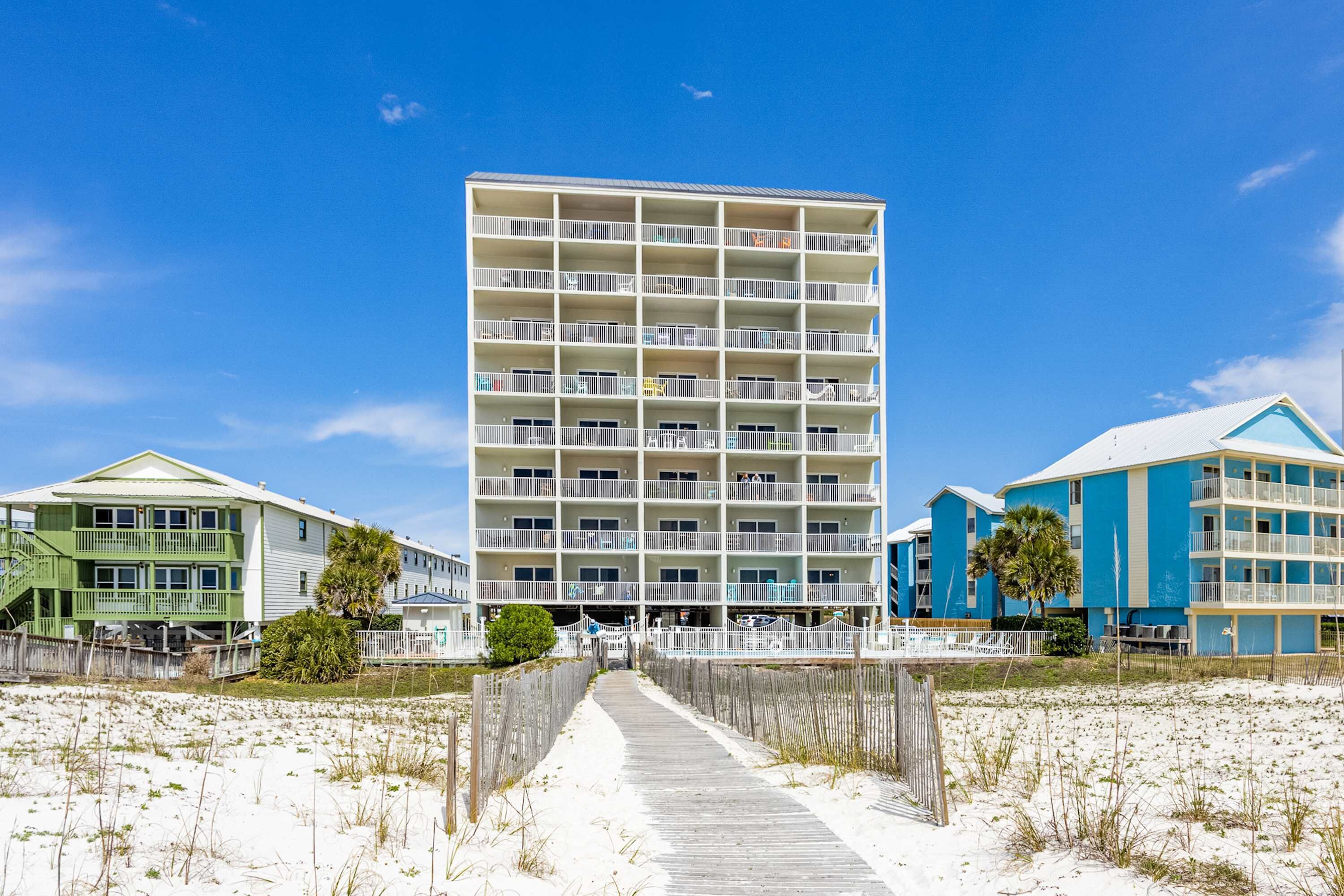 Un hotel frente al mar con varios balcones, un paseo marítimo de madera y un cielo azul despejado.