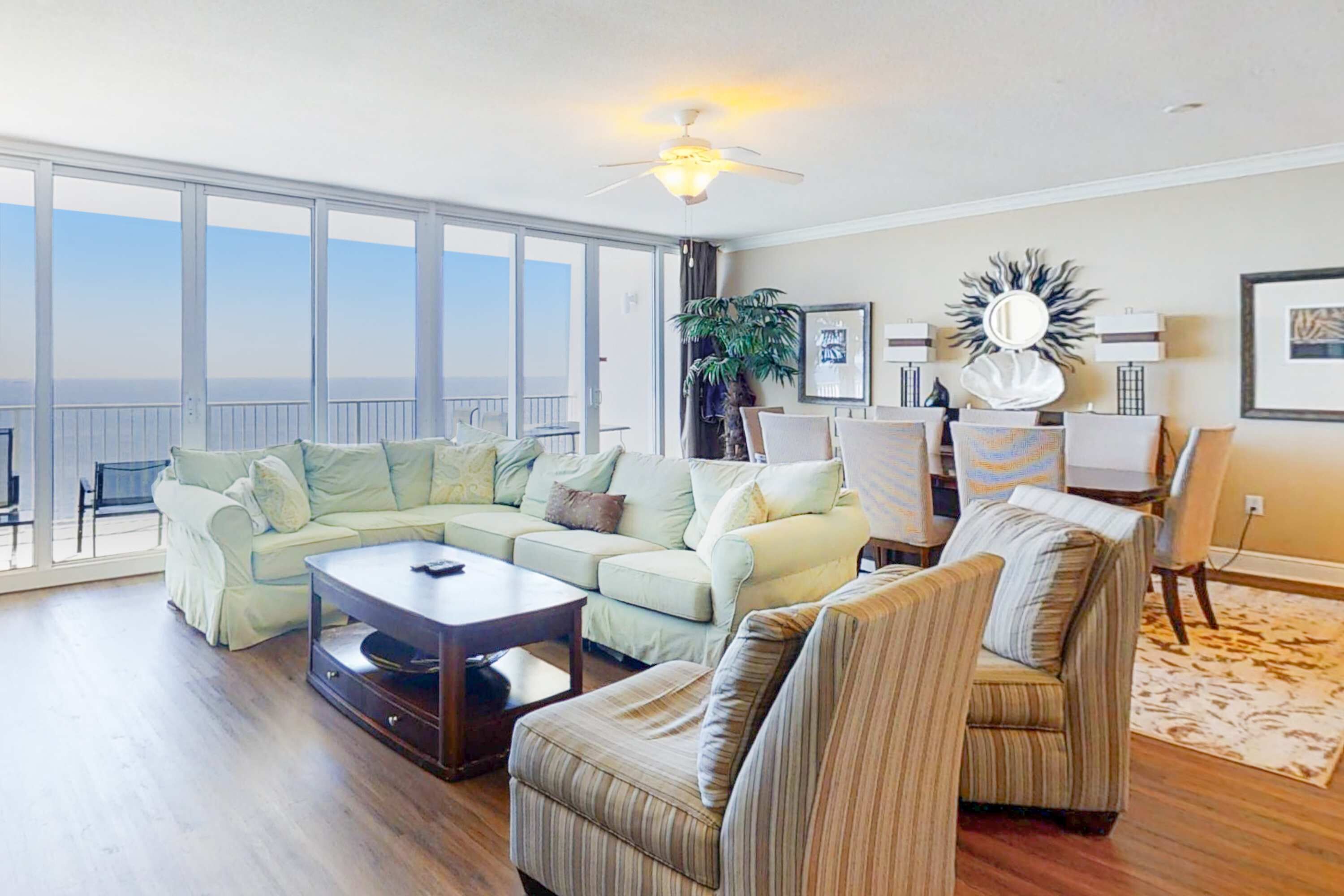A spacious living room with a large window, a ceiling fan, and a view of the ocean.
