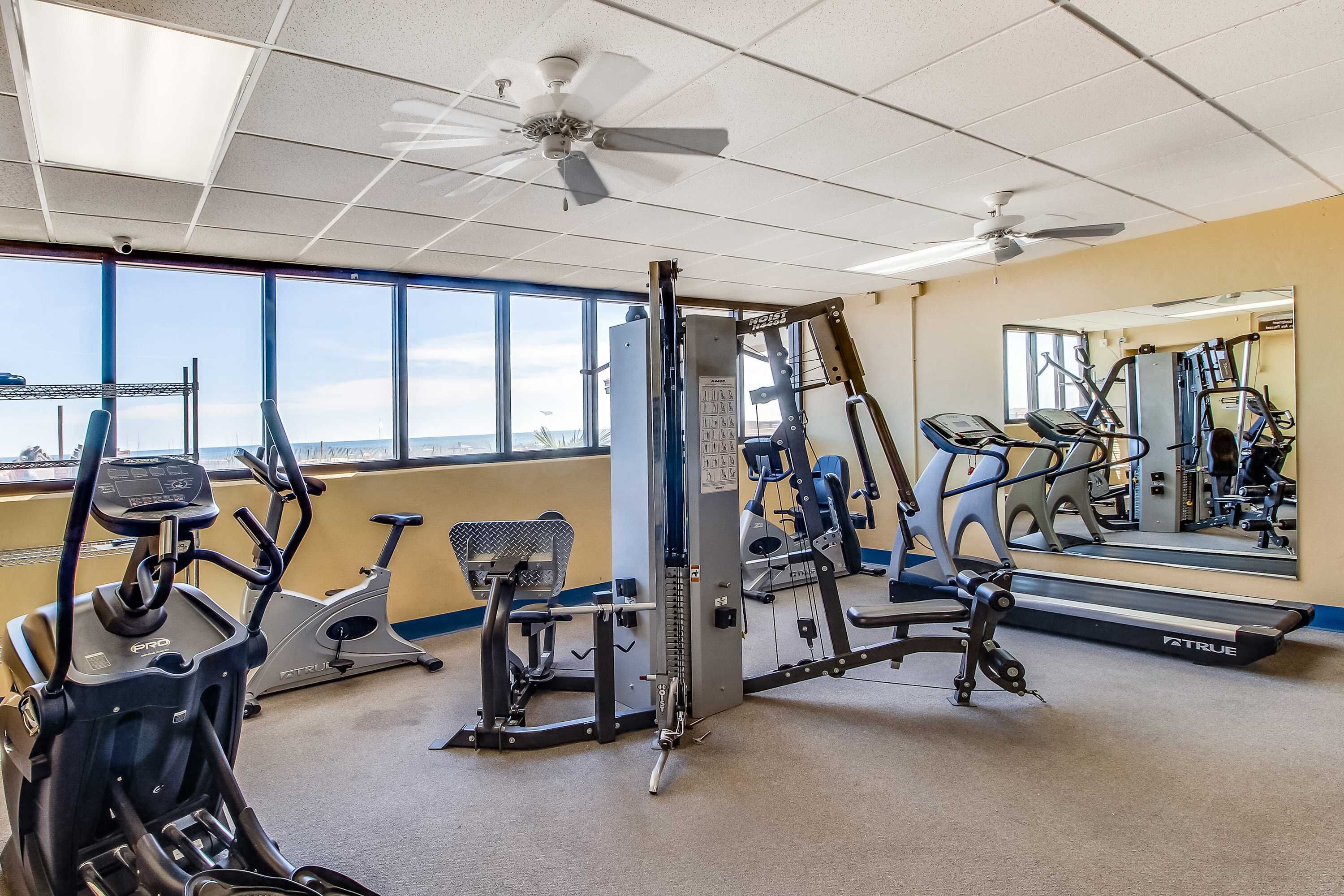 Een fitnessruimte met cardioapparatuur, losse gewichten en een spiegelwand.