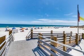 A wooden staircase leading to a beach area with umbrellas and a flag. - Casual beachfront getaway with pool, ocean views, & beach access (Orange Beach)