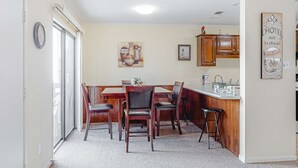 Un comedor con una mesa y sillas de madera, una cocina con armarios de madera, y un reloj fijado en la pared.