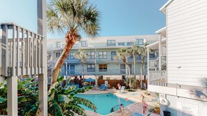 Zona de piscina con sillones de descanso, una palmera y un edificio con balcones.