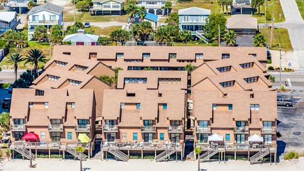 Un hotel de varios pisos con balcones, vista a la playa y zona de estacionamiento.