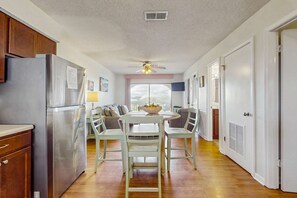 A kitchen with a refrigerator, a dining table with chairs, a ceiling fan, and a window with a view. - Lakeview Condo with Shared Pool - Just Steps from the Beach! (Gulf Shores)