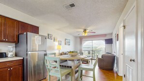 Une cuisine équipée d’un réfrigérateur, de meubles de rangement en bois, d’une table à manger avec des chaises, d’un ventilateur de plafond et offrant une vue par une fenêtre.