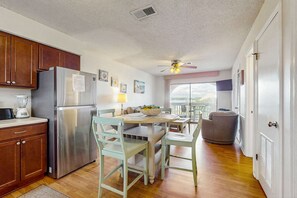A kitchen with a refrigerator, wooden cabinets, a dining table with chairs, a ceiling fan, and a view through a window. - Lakeview Condo with Shared Pool - Just Steps from the Beach! (Gulf Shores)