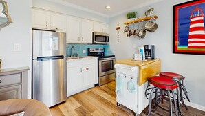 A modern kitchen with stainless steel appliances, white cabinets, a microwave, a dishwasher, and a bar area with stools. - Coastal condo close to the beach with balcony - walk everywhere! (Gulf Shores)