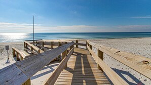 Ein Holzsteg führt zu einem Strand mit blauem Himmel und ruhiger See.