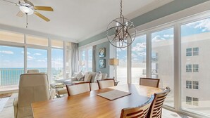 Ein geräumiger Essbereich mit einem großen Holztisch und Stühlen, einem Deckenventilator und großen Fenstern mit Blick auf den Ozean.