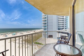 A balcony with a view of the beach and ocean, a glass table, and two chairs. - Beachfront condo with pool, private balcony, & washer and dryer (Gulf Shores)