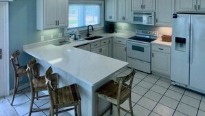 Una cocina con armarios blancos, una isla grande, sillas de madera, un fregadero, un microondas y un refrigerador.