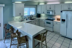 A kitchen with white cabinets, a large island, wooden chairs, a sink, a microwave, and a refrigerator. - Coastal duplex w multi-levels, shared pool and close to beach (Gulf Shores)