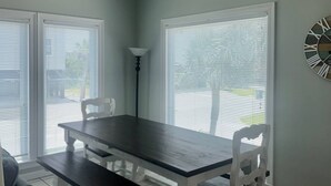 Un comedor con mesa y sillas, ventanas amplias y un reloj de pared.