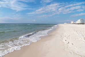 A beach with a sandy shore, ocean waves, and a row of white buildings. - The Dunes 603 | Beachside Condo with Gulf Views and Swim-Through Pool (Gulf Shores)