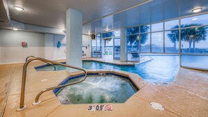 Una piscina interior con un jacuzzi, paredes de vidrio transparente y vistas a palmeras.