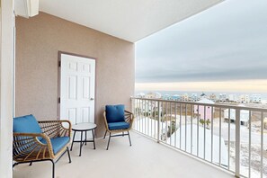 Een balkon met rieten meubels, een witte deur en uitzicht op gebouwen.