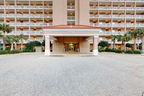 A multi-story hotel with a central entrance, numbered 1380, surrounded by palm trees and a parking area. - The Dunes 603 | Beachside Condo with Gulf Views and Swim-Through Pool (Gulf Shores)