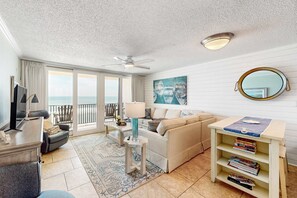 A living room with a sofa, a coffee table, a TV, a bookshelf, and a balcony with a view.