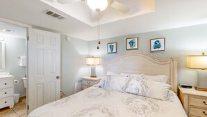 Een slaapkamer met een bed, nachtkastjes, een lamp, een plafondventilator en een deur.