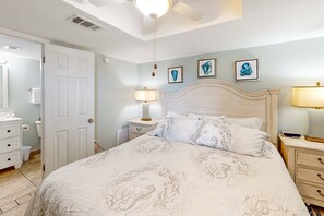 A bedroom with a bed, bedside tables, a nightstand, a lamp, a ceiling fan, and a door.