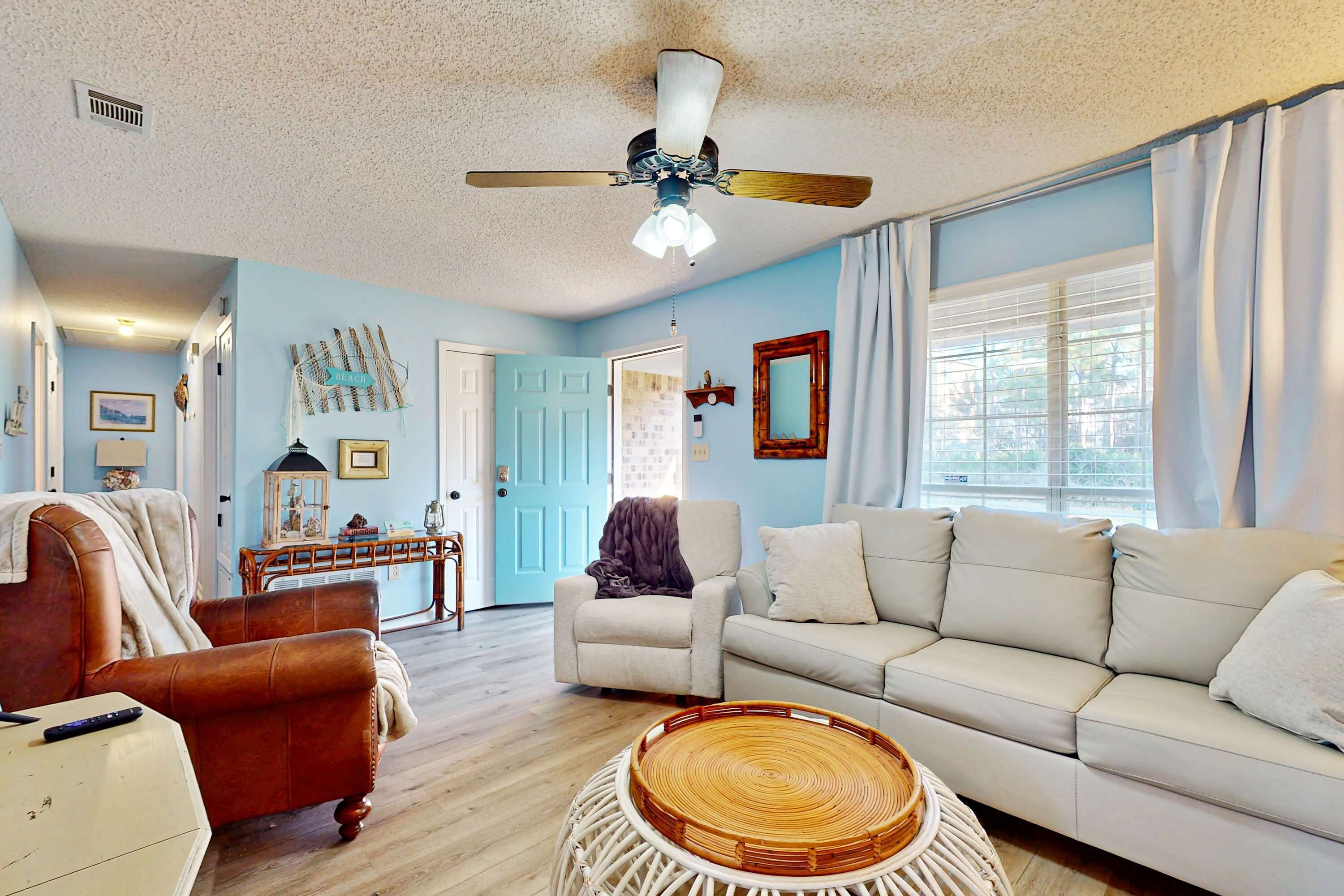 A living room with a white sofa, a brown leather chair, a ceiling fan, and a wicker coffee table.