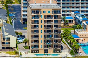 A multi-story hotel with balconies, a swimming pool, and a parking area. - Beachfront condo with shared pool, outdoor shower, and beach access (Gulf Shores)