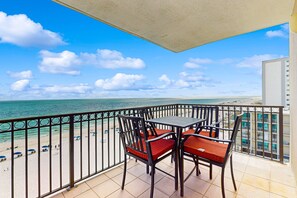 A balcony with a view of the beach and ocean, featuring a table and chairs. - Beachfront condo with shared pool, outdoor shower, and beach access (Gulf Shores)