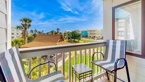 A balcony with two chairs, a small table, and a view of neighboring buildings and greenery. - Pool view studio with onsite sauna, beach access, and pickleball courts (Gulf Shores)